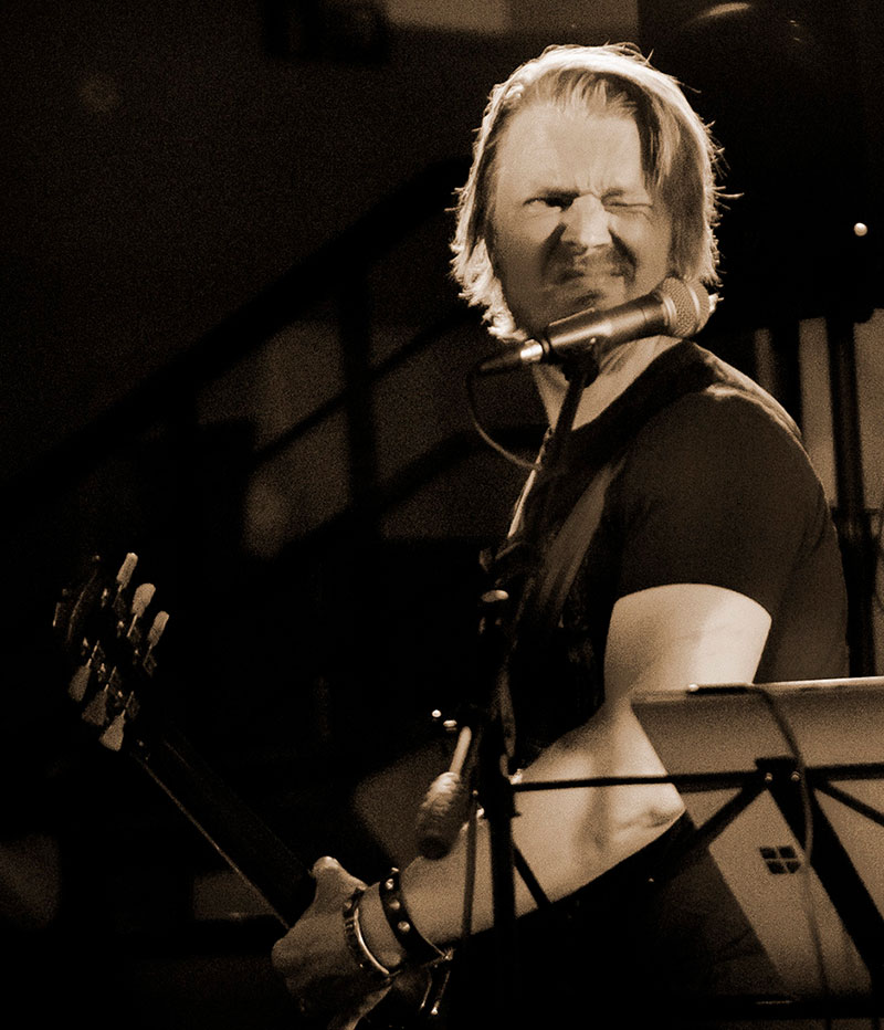 Mies soittaa kitaraa ja siristää toista silmäänsä.