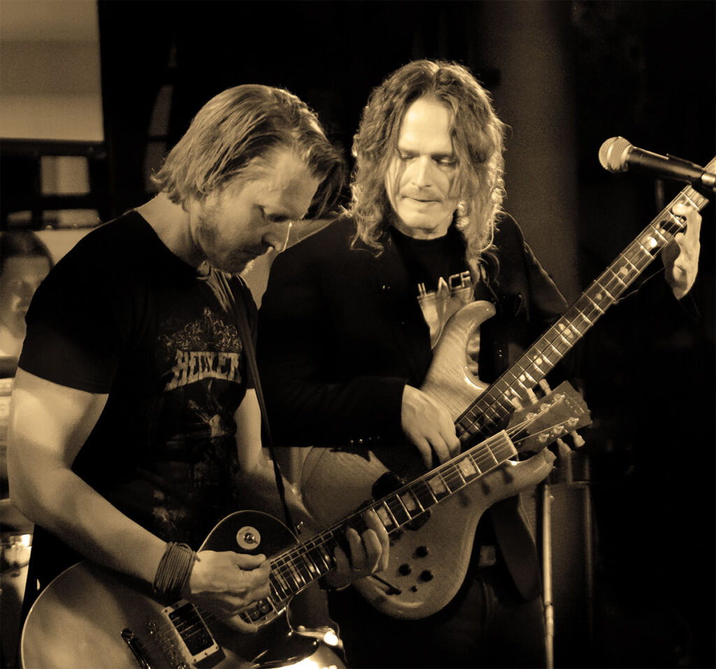 Kitaraa ja bassoa soittavat miehet seisovat vierekkäin lavalla.