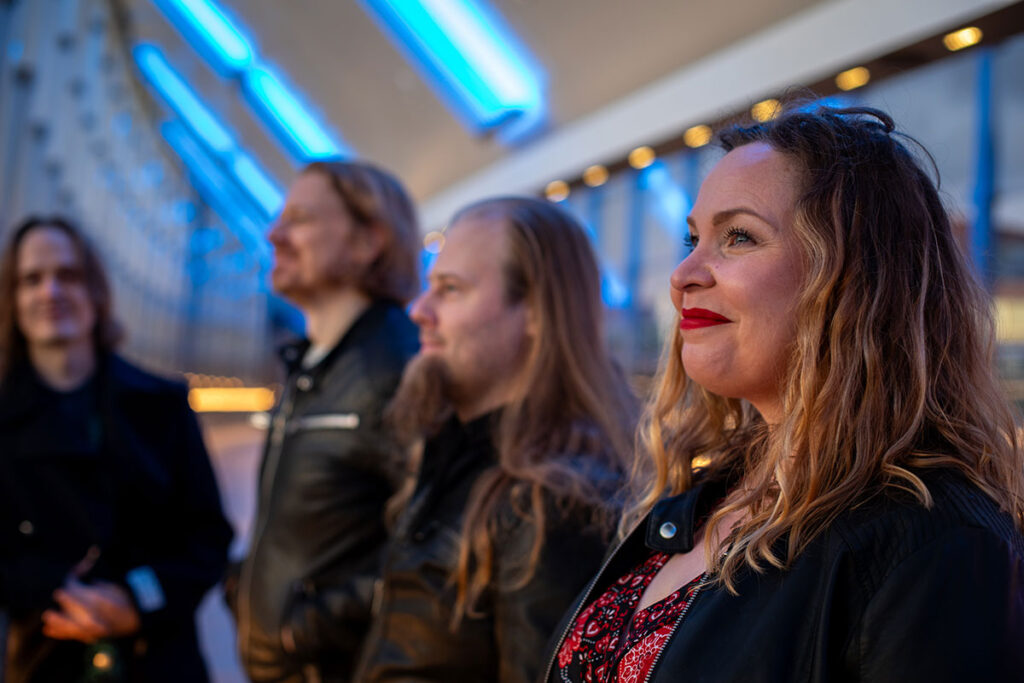 Hymyilevä nainen ja kolme miestä rivissä sivusta kuvattuna.